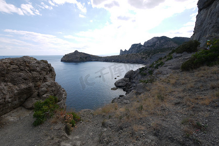 蓝色背景长图摄影照片_宽阔的海湾四周环绕着高高的克里米亚岩石，上面长满了草