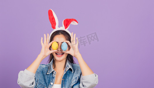 微笑的女人戴着兔耳和牛仔布，前眼拿着五颜六色的复活节彩蛋