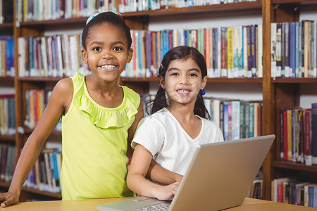 微笑的学生在图书馆使用笔记本电脑