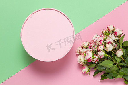 双色背景摄影照片_粉色圆形礼盒，粉色和绿色双色背景上的一束小玫瑰，复制空间，平躺。 