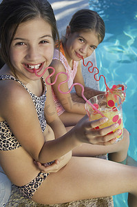 两个可爱的姐妹在游泳池边用疯狂的吸管喝果汁的肖像