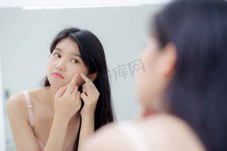 科幻青春摄影照片_美丽的亚洲年轻女性照镜子摸脸是痤疮、青春痘治疗、美女问题美容和家里房间面部皱纹的皮肤、化妆和美容概念。