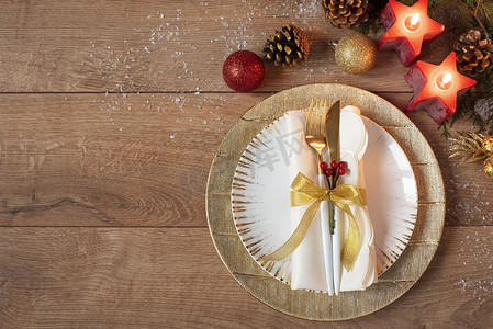 圣诞假期晚餐餐位布置-盘子、餐巾、餐具、橡木桌背景上的金色摆设装饰。