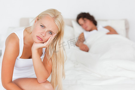 不快乐的女人坐在床上，而她的未婚夫正在睡觉