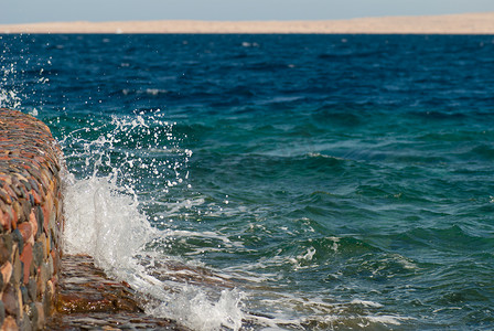 美丽清澈的绿松石海水面照片，石质海景背景上有波纹和明亮的飞溅，水平图片