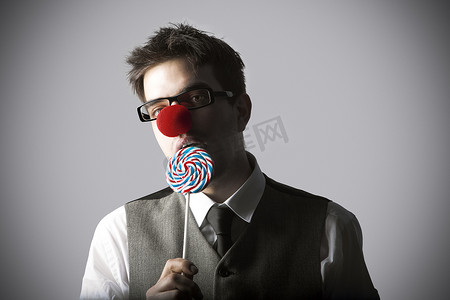 小丑鼻子吃棒棒糖的年轻时尚男人的滑稽肖像