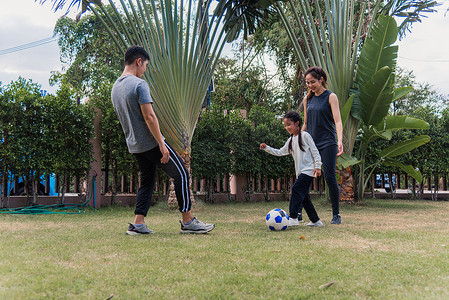 母亲、父亲和孩子的女儿在大自然的户外花园公园踢足球