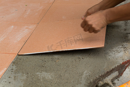 贴瓷砖摄影照片_泥水工在家贴瓷砖，瓷砖地板粘合剂翻新