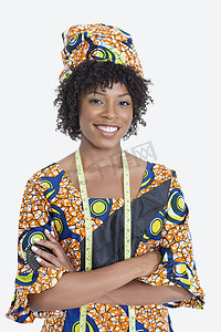 身着非洲印花服装的年轻女时装设计师站立双手折叠在灰色背景上的肖像