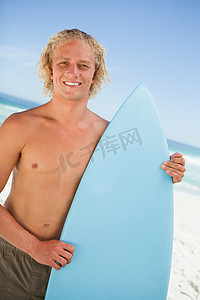 直20摄影照片_年轻的微笑男子站直，同时拿着他栖息的冲浪板