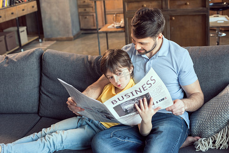 专注的儿子在家给父亲看报纸