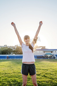 站在跑道上的年轻运动女孩举起双臂