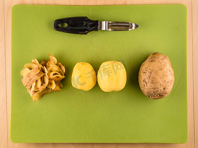 绿色塑料板上的土豆、皮和削皮器