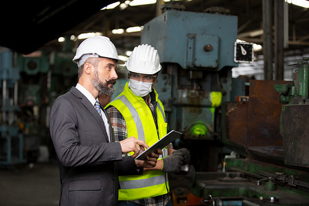 总监摄影照片_业务总监和机械工程师在工厂车间检查和讨论。