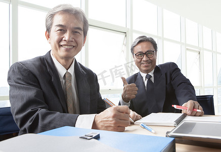 两个亚洲商人露齿笑脸，在办公室放松