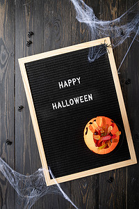 万圣节假期糖果，黑色字母板，上面写着 Happy Halloween flat，黑色木质背景，蜘蛛网