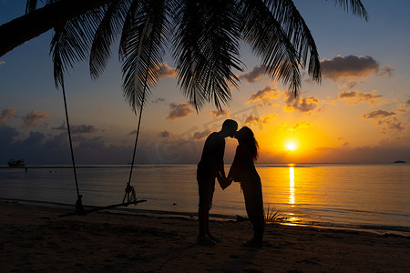 日落时在海滩上热吻的剪影情侣。