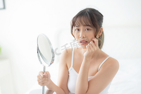 美丽的亚洲年轻女性照镜子，脸上有粉刺问题