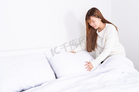 卧室毛毯摄影照片_美丽的亚洲女人一大早就在房间里整理床铺。