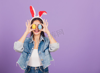 微笑的女人戴着兔耳和牛仔布，前眼拿着五颜六色的复活节彩蛋