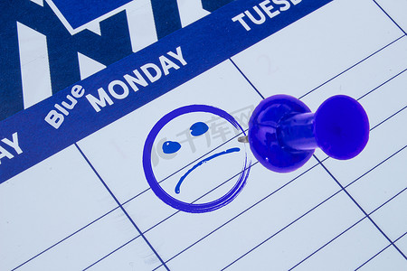 日历上的特写，聚焦于蓝色星期一，脸上有悲伤的脸和蓝色的别针