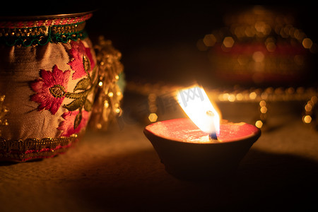 油灯摄影照片_锁定镜头显示印度排灯节上一盏 diya 油灯亮着，背景中有美丽的散景，附近有装饰品