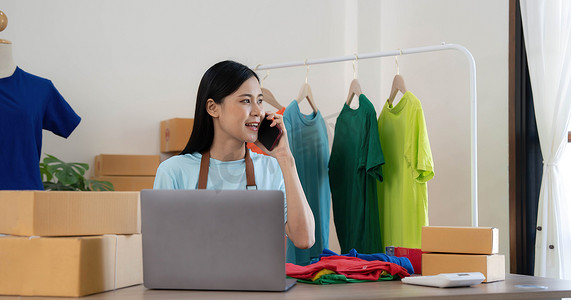 美丽的亚洲女性在线卖家通过电话确认客户的订单，创办小型企业的中小企业主女企业家在家里使用笔记本电脑、包装和交付情况概念。