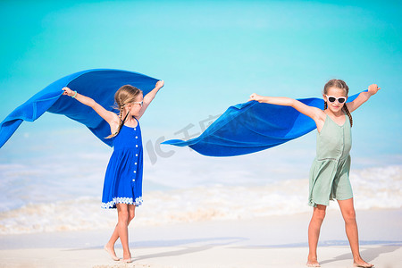 小女孩们用毛巾跑步玩得很开心，在热带海滩上用白色的沙滩和碧绿的海水享受假期