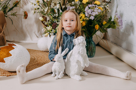 两个女孩在一个美丽的复活节照片区，那里有鲜花、鸡蛋、小鸡和复活节兔子。