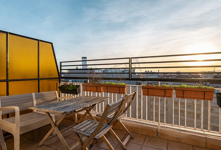 天空围栏摄影照片_宽敞的户外阳台配有舒适的木制家具，供您度过轻松的夜晚和享用美味的晚餐。