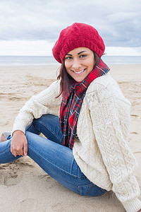 穿着时髦保暖衣服的微笑女人坐在沙滩上