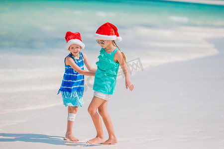 小孩圣诞老人摄影照片_圣诞海滩假期期间，可爱的小孩戴着圣诞老人的帽子。