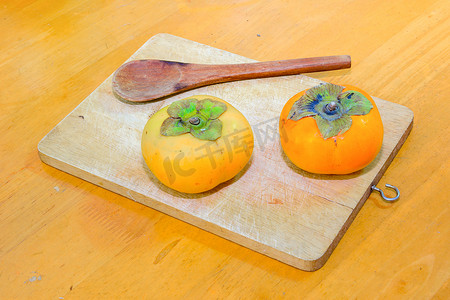 碎块摄影照片_砧板上的两个柿子和木勺