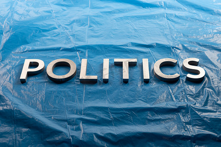 在皱巴巴的塑料蓝色胶片背景上用银色铝字放置的政治一词 - 在图片的中央
