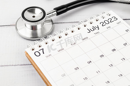 医疗听诊器和 2023 年 7 月木制背景台历，计划检查健康概念。
