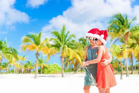 可爱的小孩戴着圣诞帽在沙滩上庆祝圣诞节玩得很开心