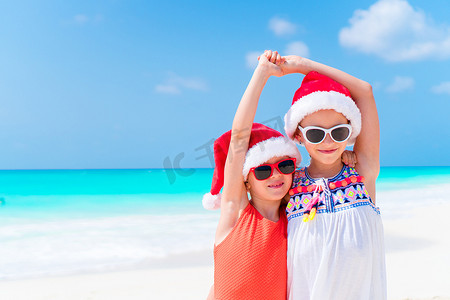 小孩圣诞老人摄影照片_圣诞海滩假期期间，可爱的小孩戴着圣诞老人的帽子。