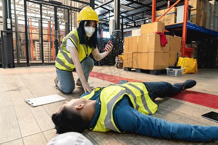 一名女仓库工人用对讲机呼叫工厂急救队，营救一名失去知觉的男子。