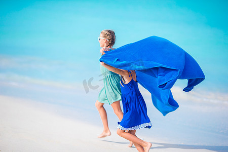 沙滩上的孩子摄影照片_在白色沙滩和碧绿海水的热带海滩上享受假期的小女孩们玩得很开心