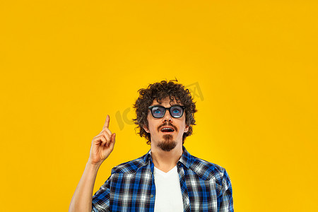画像手摄影照片_留着卷发的留着胡须的男人用手指指着在黄色背景下隔离的复制空间的画像。