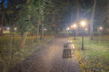 在雨天、湿漉漉的后面，灯笼和长椅散焦的夜间公园