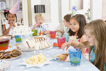 打地鼠游戏摄影照片_派对上的年幼孩子坐在桌边，面带微笑地吃着食物