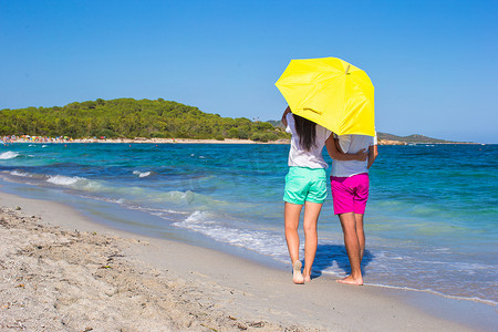 带黄色雨伞的白色沙滩上浪漫情侣的背影