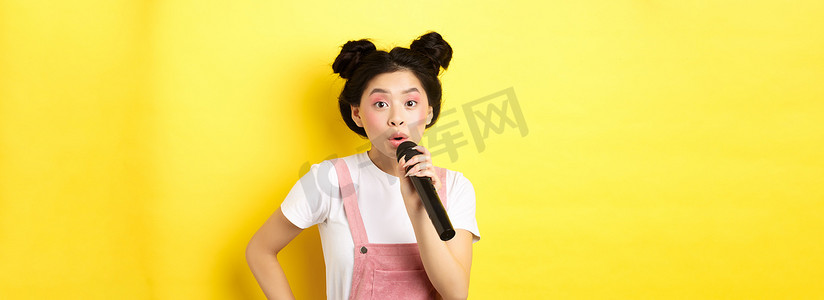 可爱的亚洲少女，妆容鲜艳，在麦克风卡拉 OK 里唱歌，站在黄色背景下