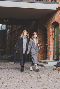 戴着医用口罩的年轻漂亮女孩朋友在城市的秋天晚上在户外玩得开心，笑着发疯 — 流行病概念的终结