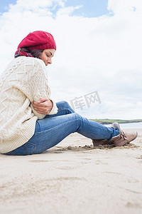 穿着时尚保暖衣服的女人坐在沙滩上