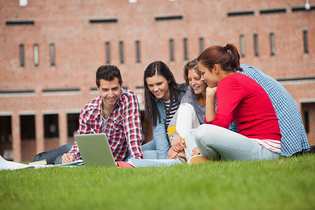 五名休闲学生坐在草地上看笔记本电脑