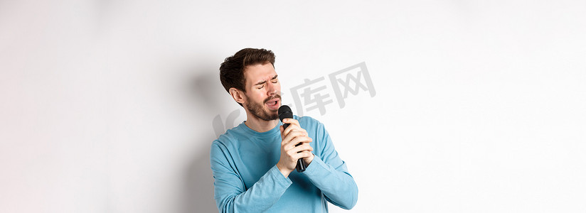 站在白色背景上的浪漫男人在卡拉 OK 用麦克风唱歌