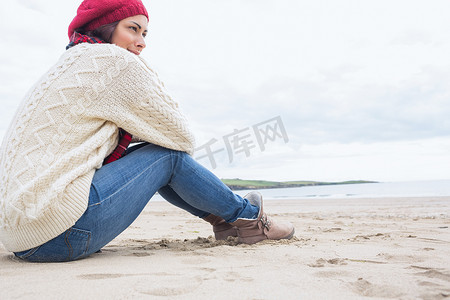 穿着时尚保暖衣服的女人坐在沙滩上