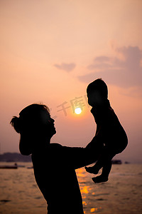 背头摄影照片_母亲的剪影在夕阳下和她蹒跚学步的孩子玩耍。
